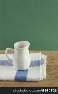 White jug and dishcloth on old wooden table over green background