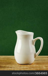 White jug on old wooden table over green background