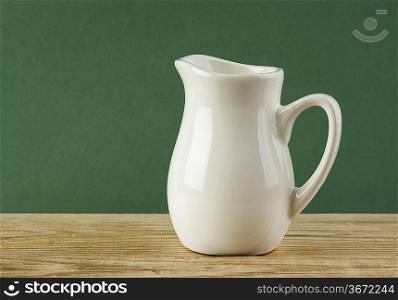 White jug on old wooden table over green background