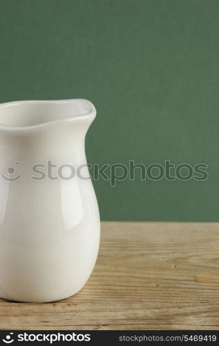 White jug on old wooden table over green background