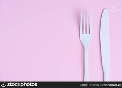 White knife and fork on trendy soft pink pastel paper background