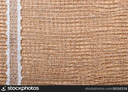 White lace ribbon on brown mesh material, natural burlap background