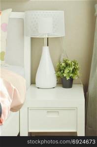 White lamp and flower pot on bedside table next to bed
