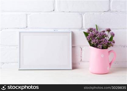 White landscape frame mockup with purple flowers in polka dot pi. White metal landscape frame mockup with purple field flowers in polka dot pink rustic pitcher vase. Empty frame mock up for presentation artwork. Template framing for modern art.