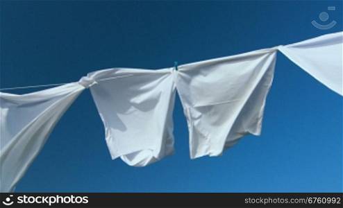 White laundry drying on clothesline against blue sky
