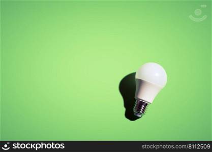 White lightbulb on green background under the bright light with black shadow.