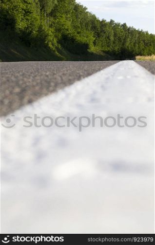 white line road markings on the new asphalt, summer landscape on the road, trees in the forest, the view of the road from below into the distance. white line road markings