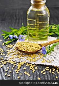 White linen seeds in a spoon, flax stalks with blue flowers and leaves on burlap, oil in a bottle on wooden board background
