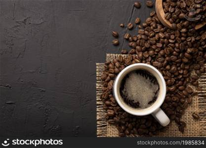 White lungo cup with hot coffee drink and toasted coffee beans scattered on a rustic black table. Top view with Copy space for your text