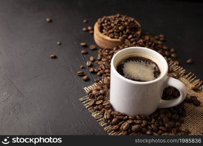 White lungo cup with hot coffee drink and toasted coffee beans scattered on a rustic black table. Copy space for your text