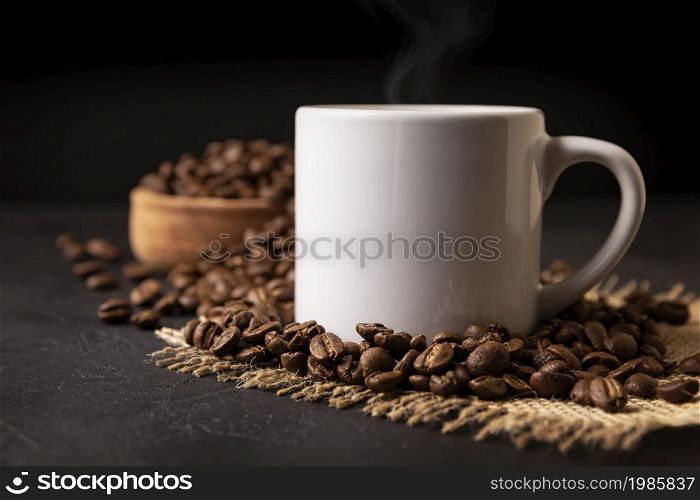 White lungo cup with hot coffee drink and toasted coffee beans scattered on a rustic black table. Close up image. Blank cup for copy space