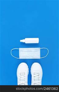 White medical mask, trainers, and hand sanitizer on a blue background. Monochrome vertical flat lay.. White medical mask, trainers, and hand sanitizer on blue background. Monochrome vertical flat lay.