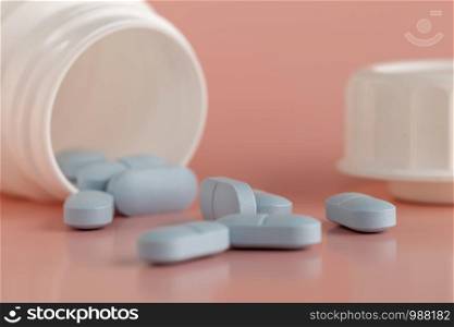 White medicine bottle and blue pills on a pink background. Close-up.. Medicine bottle and blue pills on a pink background.
