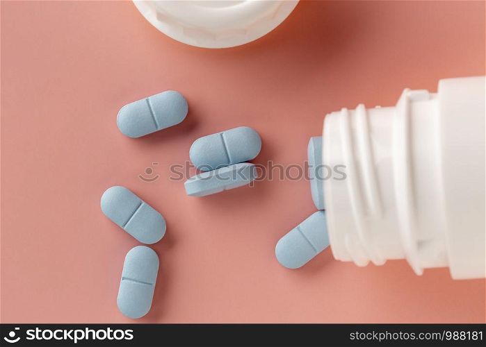 White medicine bottle and blue pills on a pink background. Top view. Medicine bottle and blue pills on a pink background.