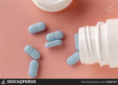 White medicine bottle and blue pills on a pink background. Top view. Medicine bottle and blue pills on a pink background.