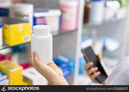 white medicine bottle and smartphone in hand pharmacist and medicine shelves background