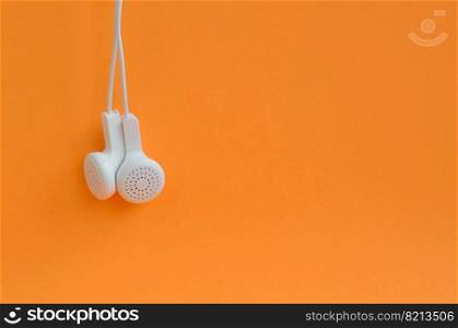 White modern headphones hanging on a bright orange background. A template for music listening fans. White modern headphones hanging on a bright orange background