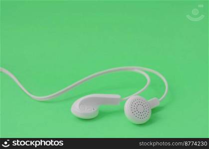White modern headphones lie on a bright green background. A template for music listening fans. A template for music listening fans. White earphones on green