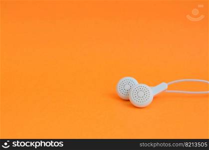 White modern headphones lie on a bright orange background. A template for music listening fans. White modern earphones lies on a bright orange background.