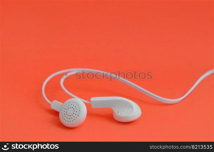 White modern headphones lie on a bright red background. A template for music listening fans. A template for music listening fans. White earphones on red