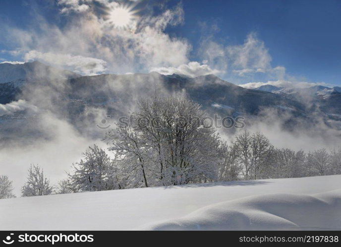 white mountain landscape  covered with snow  in front of cloudy sky  illuminated by the sun
