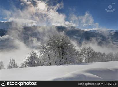 white mountain landscape  covered with snow  in front of cloudy sky  illuminated by the sun