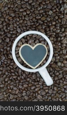 White mug and wooden heart shape on coffee beans background&#xA;
