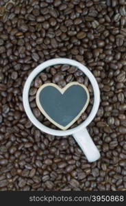 White mug and wooden heart shape on coffee beans background&#xA;