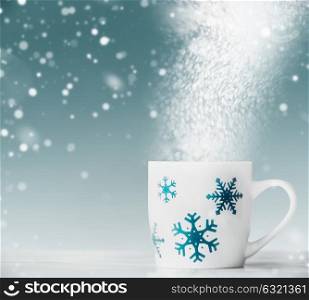 White mug with blue snowflakes on white table at blue background with snow and bokeh, front view. Happy winter holiday card layout