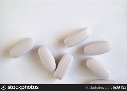 White or light grey long vitamins or pills on white background, macro, close-up, copy space, flatly. Nutritional supplements concept, health, vitamins, monochrome minimal style. Horizontal.