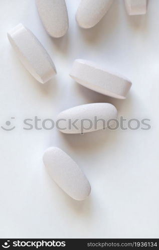 White or light grey long vitamins or pills on white background, macro, close-up, copy space, flatly. Nutritional supplements concept, health, vitamins, monochrome minimal style. Vertical.