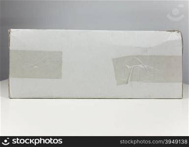 White packet parcel. Small white packet corrugated cardboard parcel for mail shipping on a white table with elegant grey background