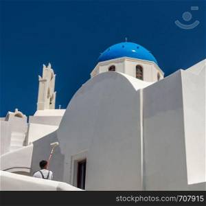 White paint being applied by roller to traditional house in Santorini. Worker repainting traditional cave house on Santorini