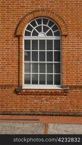 White painted wood arched window in a red brick wall .