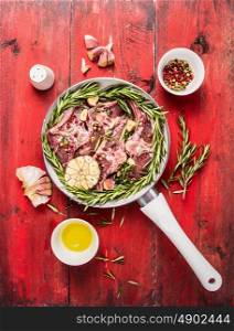 white pan with raw lamb loin chops meat , herbs,oil and spices on red wooden background, top view