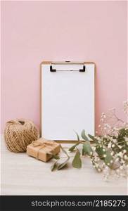 white paper clipboard with spool gift box baby s breath flowers wooden desk against pink background
