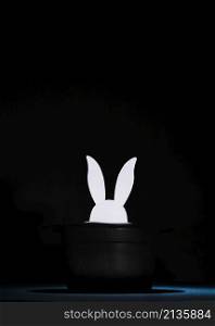 white paper cut out rabbit heads top black hat against black background