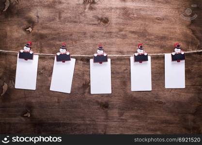 white paper tags hanging on a rope hooked on decorative christmas clothespins, brown wooden background