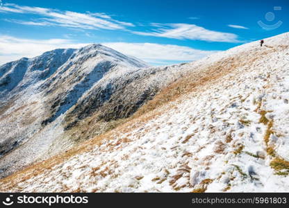 White peaks of mountains in snow and man hiking along winter landscape