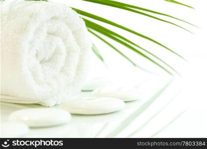 White pebbles, towel and palm leaf over white. Selective focus.