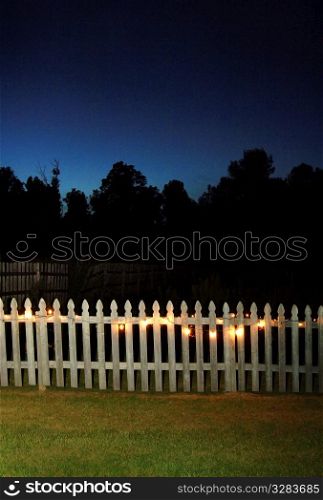 White picket fence at night with lights on.