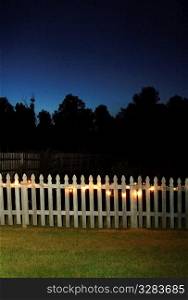 White picket fence at night with lights on.