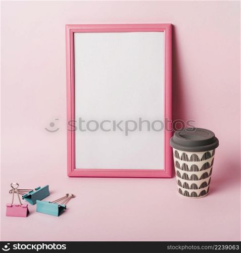 white picture frame with border paper clips coffee disposable cup against pink background