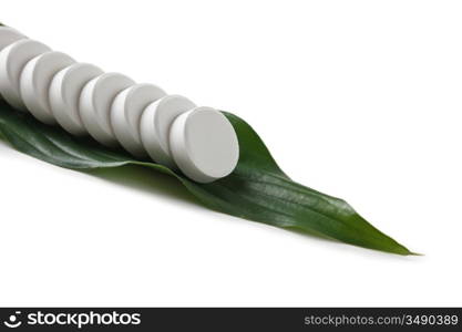 white pill lying on a green leaf isolated on a white background