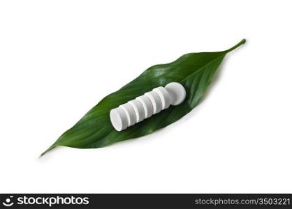 white pill lying on a green leaf isolated on a white background