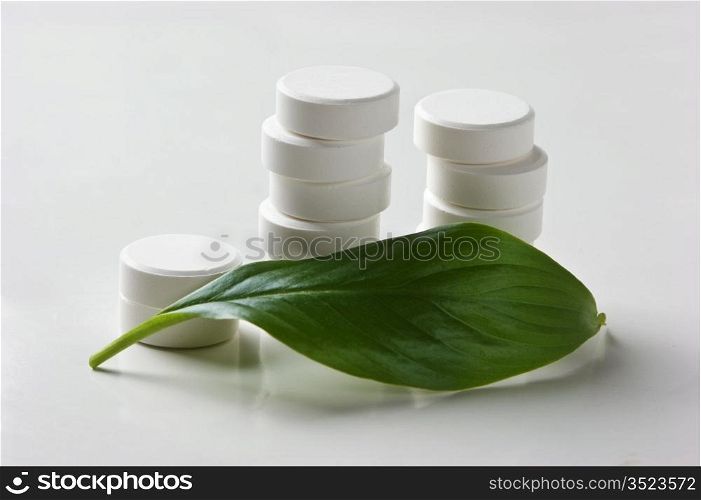white pill lying on a green leaf isolated on a white background