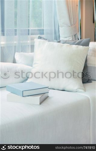 White pillows and books setting on white sofa in modern living room