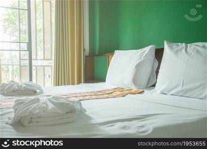 White pillows and white towels on bed in green wall room