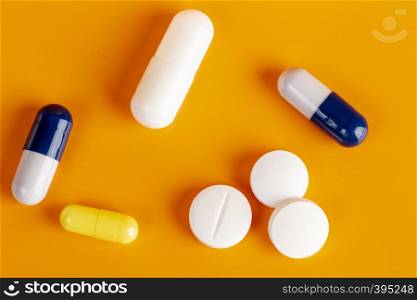 White pills and different color capsules on orange background. White round pills and color capsules
