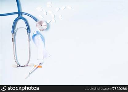 White pills, blue Diabetes Awareness Ribbon with stethoscope and blood test on blue background, copy space. White pills on blue background